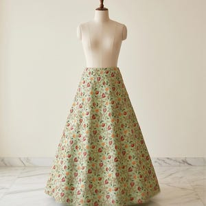 May include: A floor-length, A-line skirt in a light mint green hue, featuring an intricate, dense floral embroidery pattern in shades of deep red, burnt orange, and gold thread, displayed on a neutral-toned mannequin torso.