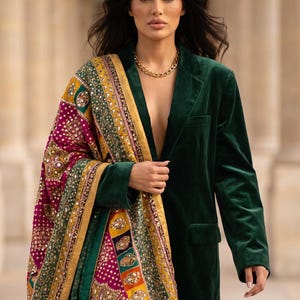 May include: A dark green velvet blazer paired with a vibrant, multi-coloured shawl featuring intricate embroidery, gold-toned borders, and reflective mirror accents. The shawl displays a rich pattern of magenta, yellow, and green fabric panels.