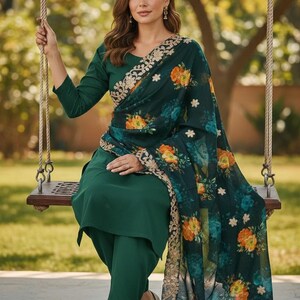 May include: A woman wearing a dark green salwar kameez, a traditional South Asian outfit, sits on a wooden swing. The outfit includes a long-sleeved top and matching pants. A floral patterned scarf with gold trim drapes over the shoulders.
