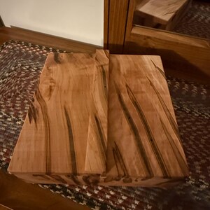 May include: A rectangular wooden block with a natural wood grain pattern. The block is light brown with dark brown streaks. The wood grain is visible on the top and sides. The block is likely for decorative use. The block is made of wood.