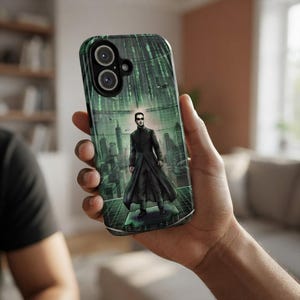 Op de afbeelding: Een smartphonehoesje met een grafische illustratie van een figuur in een lange zwarte jas en donkere zonnebril die op een platform staat. De achtergrond toont een groen digitaal matrixpatroon met een stadsgezicht en codelijnen.