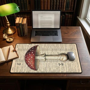 Peut inclure: Tapis de souris rectangulaire avec une illustration détaillée d'un champignon rouge et blanc. Le motif de champignon est placé sur un fond de texte de journal vintage. Une souris d'ordinateur repose sur le côté droit.