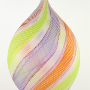 May include: A colorful glass art piece with a teardrop shape. The piece features a swirl design of orange, yellow, green, and purple stripes. The glass has a smooth, glossy finish and a pointed top.