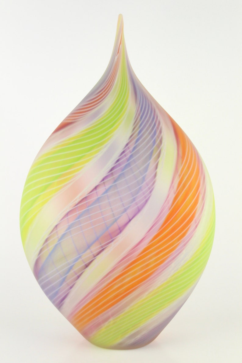 May include: A colorful glass art piece with a teardrop shape. The piece features a swirl design of orange, yellow, green, and purple stripes. The glass has a smooth, glossy finish and a pointed top.