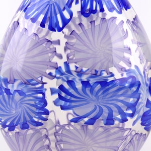 May include: A clear glass vase with a unique design. The vase features a pattern of swirling blue and lavender floral shapes. The vase has a rounded, elongated shape, and the design is visible throughout the glass.