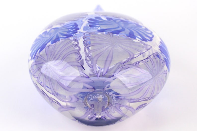 May include: A clear glass orb with a blue floral design. The orb has a rounded shape with a small, pointed top. The floral pattern is a series of swirling lines and shapes. The glass is transparent, allowing light to pass through.