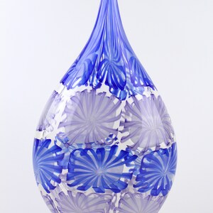 May include: A teardrop-shaped glass vase with a long, pointed top. The vase features a pattern of blue and lavender floral designs on a clear background. The top is a solid blue color.