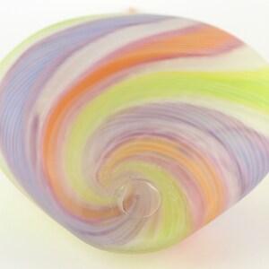 May include: A colorful, swirled glass ornament in shades of lavender, orange, white, and green. The glass has a spiral design and a small hole at the bottom. The ornament is likely for decoration.