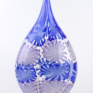 May include: A teardrop-shaped glass vase with a clear base and a pattern of blue and lavender swirls. The vase has a long, pointed top and is suitable for home decor.