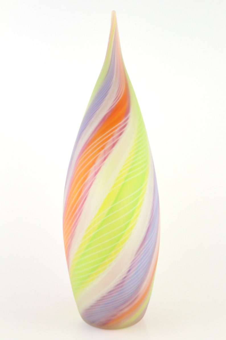 May include: A tall, teardrop-shaped glass vase with a spiraling design. The vase features bands of color including orange, yellow, green, purple, and white. The glass has a smooth, glossy finish and a pointed top.