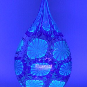 May include: A teardrop-shaped glass vase with a blue and white floral pattern. The vase has a long, slender neck and a rounded base. The floral design is composed of circular and spiral shapes, creating a unique decorative piece.