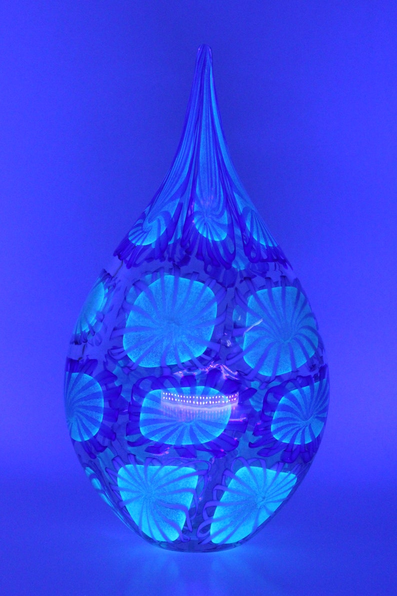 May include: A teardrop-shaped glass vase with a blue and white floral pattern. The vase has a long, slender neck and a rounded base. The floral design is composed of circular and spiral shapes, creating a unique decorative piece.