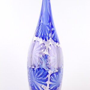 May include: A tall, decorative glass vase with a teardrop shape and a pointed top. The vase features a pattern of blue and white floral designs. The vase is approximately 12 inches tall.
