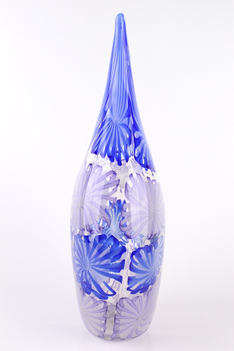 May include: A tall, decorative glass vase with a teardrop shape and a pointed top. The vase features a pattern of blue and white floral designs. The vase is approximately 12 inches tall.
