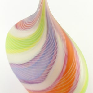 May include: A colorful, teardrop-shaped glass art piece. The sculpture features swirling bands of orange, pink, purple, green, and white. The glass has a smooth, glossy finish and a pointed top. The artwork is set against a white background.