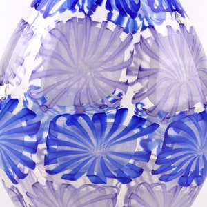 May include: A clear glass vase with a teardrop shape. The vase is decorated with a pattern of blue and lavender floral designs. The blue designs are more prominent near the top of the vase.