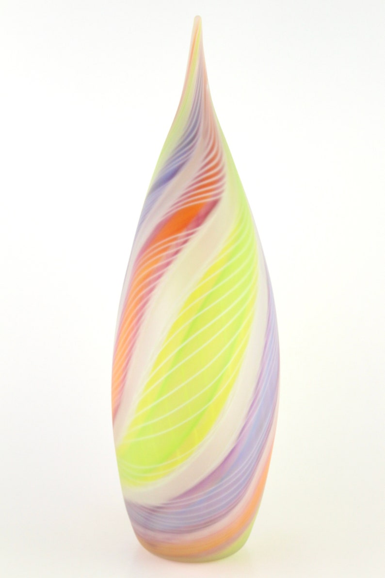 May include: A tall, teardrop-shaped glass vase with a colorful, swirled design. The vase features bands of orange, purple, yellow, and white, with thin white lines. The vase has a smooth, glossy finish and a pointed top.