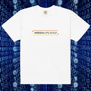 May include: A white short-sleeved t-shirt featuring the word MEGAUPLOAD printed in a dark grey font across the chest. The text is enclosed within a thin, rectangular orange border with small arrows pointing in opposite directions on the sides.