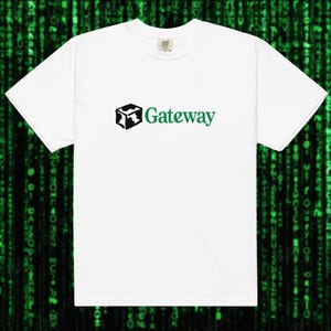 Può includere: Una t-shirt bianca a maniche corte con un logo a forma di cubo a macchie di mucca bianco e nero posizionato a sinistra della parola Gateway stampata in un carattere serif verde scuro al centro del petto.