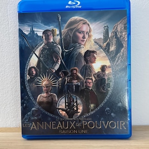 Peut inclure: Boîtier Blu-ray bleu pour "Le Seigneur des Anneaux : Les Anneaux de Pouvoir" Saison Une. La jaquette présente des personnages et un paysage fantastique. Le logo Blu-ray Disc est visible.