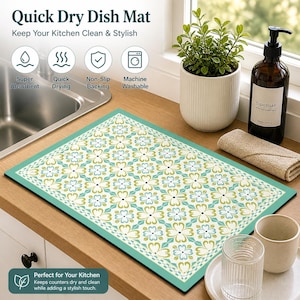 May include: A rectangular dish drying mat with a floral pattern in white, blue, and green, framed by a teal border. The mat is on a wooden countertop near a sink, with text that reads "Quick Dry Dish Mat".