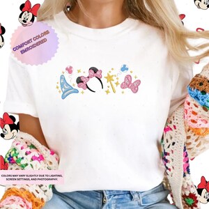 A person wearing a white t-shirt with a colorful embroidered design featuring Minnie Mouse and other Disney-themed elements.