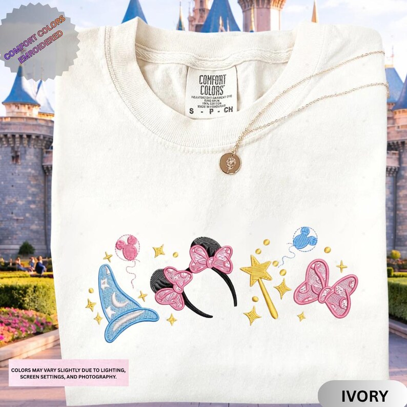A white t-shirt with a colorful embroidered design featuring a wizard hat, butterflies, and stars, along with a charm necklace.
