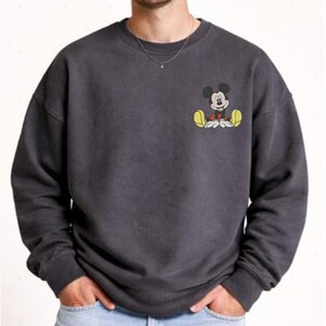 A man wearing a gray sweatshirt with a cartoon character printed on the front.