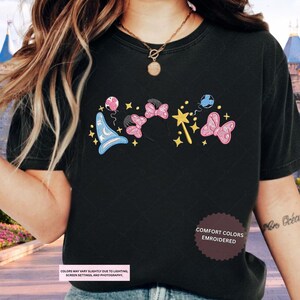 A person wearing a black t-shirt with a graphic design featuring various Disney-themed elements such as Mickey Mouse, Minnie Mouse, and a wand.