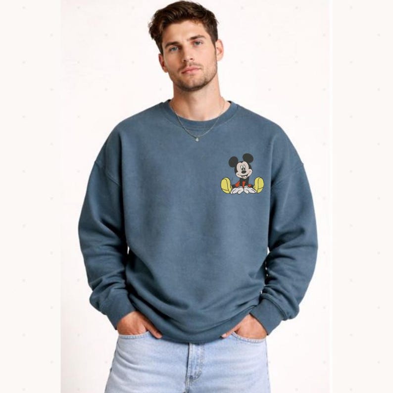 A man wearing a blue sweatshirt with a cartoon character on it, standing against a white background.