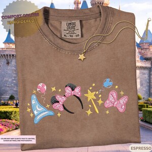 a brown t-shirt with various Disney-themed embroidered designs, including a wizard hat, butterflies, and stars.