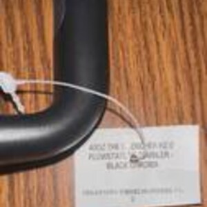 Puede incluir: Un mango de paraguas negro y curvado con una etiqueta blanca adjunta. La etiqueta tiene el texto "4002 THE T. CROCHET KEY PLUMSTAIL GARBLER BLACK ORDER". El mango es de un material liso y mate.