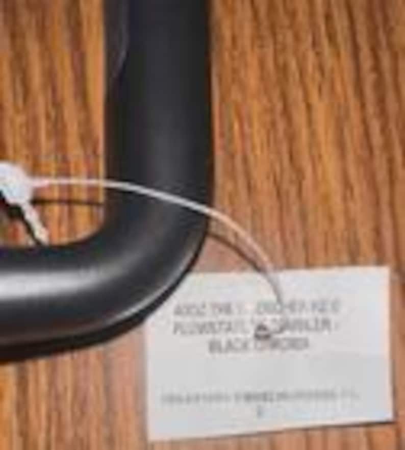 Puede incluir: Un mango de paraguas negro y curvado con una etiqueta blanca adjunta. La etiqueta tiene el texto "4002 THE T. CROCHET KEY PLUMSTAIL GARBLER BLACK ORDER". El mango es de un material liso y mate.