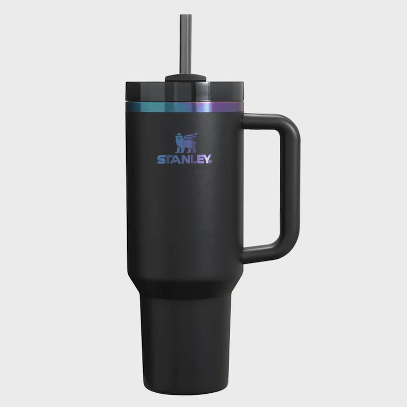 Puede incluir: Vaso Stanley negro con asa y pajita. El vaso tiene una tapa negra con una banda iridiscente hologr&aacute;fica. El logotipo de Stanley es visible en la parte delantera. Este termo de viaje aislado est&aacute; dise&ntilde;ado para mantener las bebidas fr&iacute;as durante horas.