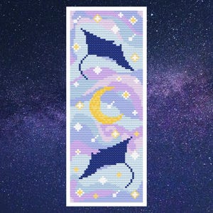 May include: A handmade bookmark featuring a celestial design. The bookmark showcases two dark blue manta rays, a yellow crescent moon, and white stars against a background of light blue, purple, and white. The bookmark is rectangular with a white border.