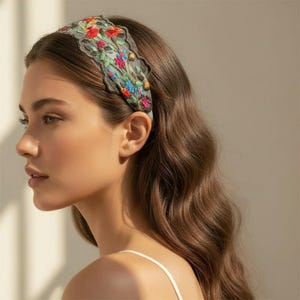Può includere: Una fascia per capelli larga con una base in rete grigia trasparente e un intricato ricamo floreale in tonalità vivaci di rosso, blu, verde e giallo. I bordi del tessuto presentano un design smerlato e il ricamo copre la superficie.