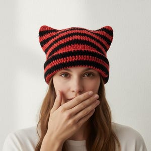 May include: A red and black striped cat ear beanie. The hat is crocheted with alternating stripes of red and black. The beanie has two pointed cat ears on top.