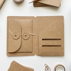 Peut inclure: Un organisateur en papier kraft marron avec une poche, une enveloppe et une fermeture à cordon. L'organisateur est ouvert, révélant l'intérieur. Des articles de papeterie supplémentaires, dont un crayon, du ruban adhésif et du papier, sont éparpillés.