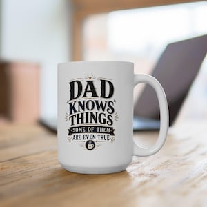 Peut inclure: Un mug en céramique blanche avec une anse, portant l'inscription en noir et doré DAD KNOWS THINGS SOME OF THEM ARE EVEN TRUE, agrémenté de fioritures décoratives et d'une petite icône de tasse à café avec une étoile au centre en bas.