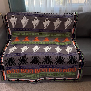 May include: A handmade Halloween crochet blanket. The blanket has a grey background with white ghosts, black spiders, and orange jack-o'-lanterns. The word "BOO" is displayed in orange. The border is green, black, and orange.