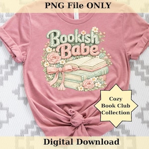 以下が含まれることがあります： フローラルデザインの「Bookish Babe」という文字が入ったピンク色のTシャツ。グラフィックには、開いた本、本の山、リボンが含まれています。このシャツには、「Cozy Book Club Collection」と「Digital Download」という文字も入っています。