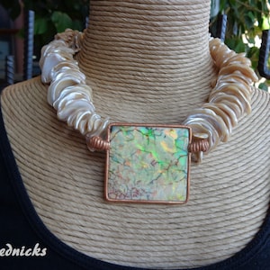 May include: A white shell necklace with a square iridescent green and blue pendant. The pendant is set in a copper frame.