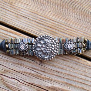 May include: A silver bracelet with a large, ornate, silver charm in the center. The bracelet is made of small, silver and black beads.