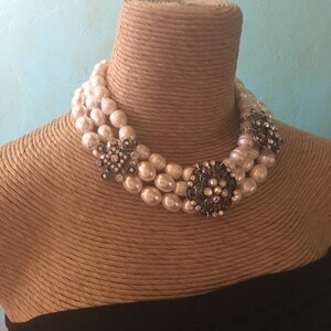 May include: A three-strand pearl choker necklace with two large silver and rhinestone brooches.