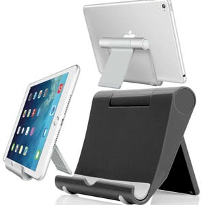 May include: A silver tablet computer resting on a foldable silver stand, and a separate black foldable tablet stand. The tablet screen displays a grid of colorful application icons. The stands feature a hinged design for adjustable viewing angles.