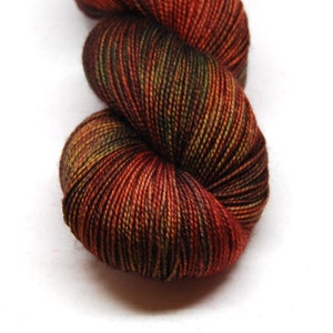 Puede incluir: Un ovillo de hilo en tonos de rojo, naranja, marrón y verde. El hilo está retorcido en forma de espiral.