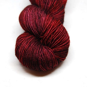 May include: A skein of deep red and black yarn with a subtle ombre effect. The yarn is soft and smooth, and it has a slight sheen.