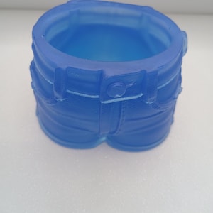 May include: A translucent blue container shaped like a pair of denim shorts. The container has details such as belt loops, pockets, and a button closure. The open top allows for storage of small items.