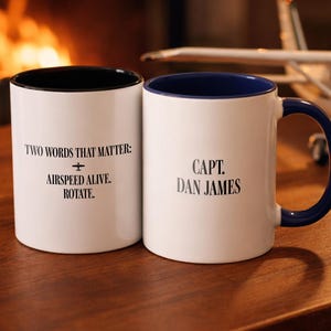 May include: Two white ceramic mugs with black and blue accents. One mug reads "TWO WORDS THAT MATTER: + AIRSPEED ALIVE. ROTATE." The other mug says "CAPT. DAN JAMES."