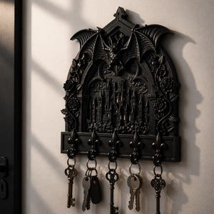May include: Black gothic key holder featuring a castle and dragon design. The key holder has five hooks with fleur-de-lis ends, holding keys. The wall-mounted holder is made of a dark material and decorated with roses. A decorative item.